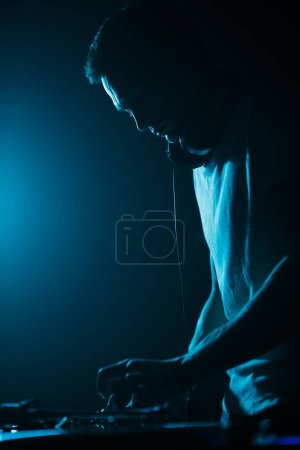 Photo for Silhouette of DJ playing music on party in night club. Disc jockey mixing vinyl records on stage - Royalty Free Image