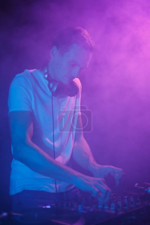 Téléchargez les photos : Club DJ joue ensemble dans les néons et la fumée. Cool jeune disc-jockey mixant de la musique sur la fête en boîte de nuit - en image libre de droit