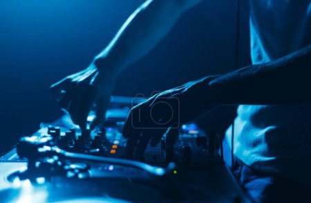 Foto de Hands of a DJ mixing music tracks with sound mixer. Close up photo of disc jockey playing set on stage in night club - Imagen libre de derechos
