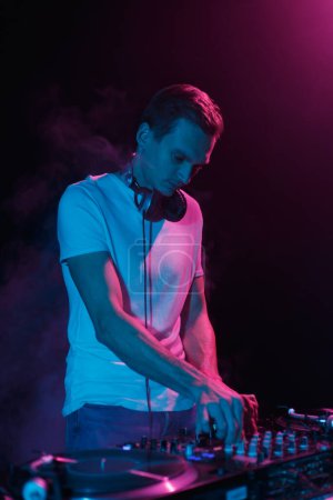 Foto de Cool joven DJ tocando música en la fiesta en luces de neón azul. Hombre blanco actuando como disc jockey en un club nocturno - Imagen libre de derechos