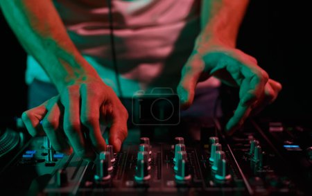 Photo for Club DJ playing music with sound mixer. Rave party disc jockey mixing musical tracks in close up - Royalty Free Image