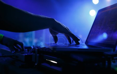 Téléchargez les photos : Club DJ jouant de la musique avec ordinateur portable et contrôleur midi. Main de disc-jockey professionnel mélangeant des pistes musicales sur la fête dans une boîte de nuit - en image libre de droit