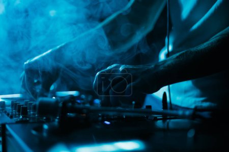 Téléchargez les photos : Hip hop dj playing music in smoke on concert. Disc jockey play musical tracks on stage in night club - en image libre de droit