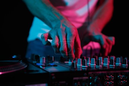 Foto de Disc jockey mixing techno music on rave party. Disk jokey adjusting volume frequency regulator on professional sound mixer device - Imagen libre de derechos