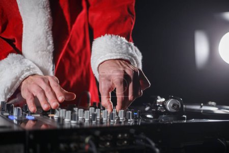Téléchargez les photos : Fête de Noël DJ en costume de Père Noël joue ensemble. Disc jockey en tenue de Noël rouge traditionnelle jouant de la musique - en image libre de droit