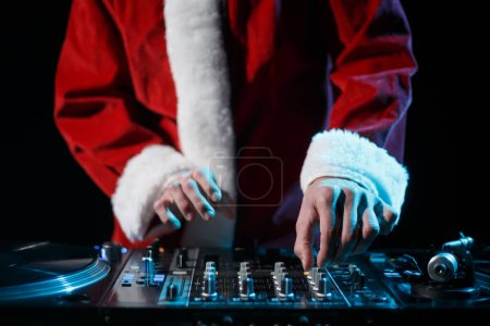 Téléchargez les photos : DJ de Noël en costume de Père Noël jouant de la musique en boîte de nuit. Disc jockey portant tenue de Noël rouge traditinal sur la fête - en image libre de droit