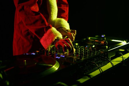 Téléchargez les photos : Santa Claus DJ mixing music set on New Year's Eve celebration in night club. Christmas party disc jockey in traditional red Xmas clothes - en image libre de droit