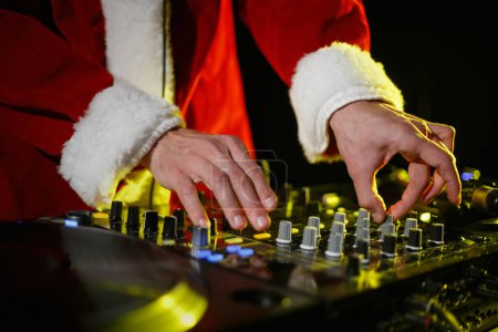 Foto de Santa DJ toca música en la fiesta de Nochevieja. Disco jockey con traje tradicional de Navidad roja mezclando pistas musicales - Imagen libre de derechos