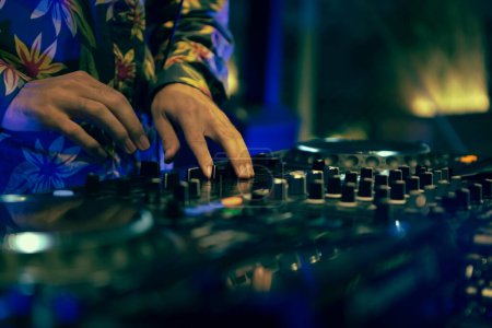 Foto de Club DJ playing music with sound mixer and cd turntables. Disc jockey mixing musical tracks with professional mixing controller on stage in night club - Imagen libre de derechos