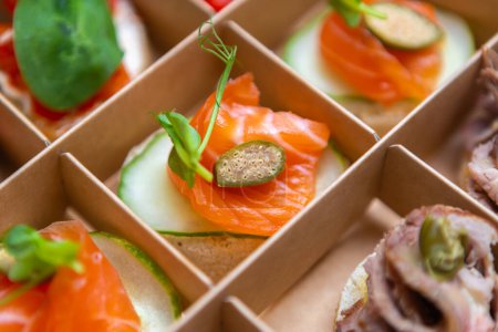 Photo for Canape snacks with red salmon fish fillet served with capers and delivered in cardboard box for food catering on venue - Royalty Free Image