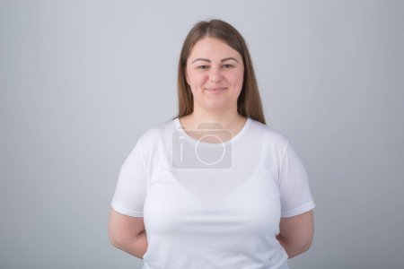 Téléchargez les photos : Cheerful plus size model posing in studio. Young Caucasian overweight woman wearing white t-shirt looking in camera with a smile - en image libre de droit