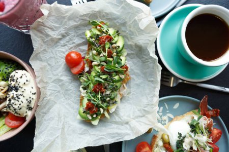 Téléchargez les photos : Délicieux petit déjeuner méditerranéen servi au restaurant. Sandwich bruschetta frais à l'avocat tranché et tomates séchées servi sur la table et tiré d'en haut - en image libre de droit
