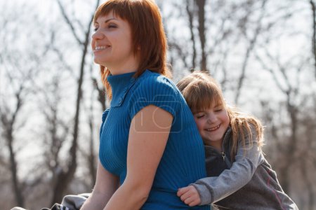Téléchargez les photos : Happy little girl hugging her mother in sunny park. Adult Ukrainian woman enjoying the weekend with her little daughter in Europe - en image libre de droit