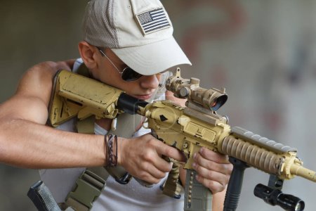 Foto de Young Ukrainian soldier aiming with modern assault rifle. Trained white male person shooting with big automatic gun - Imagen libre de derechos