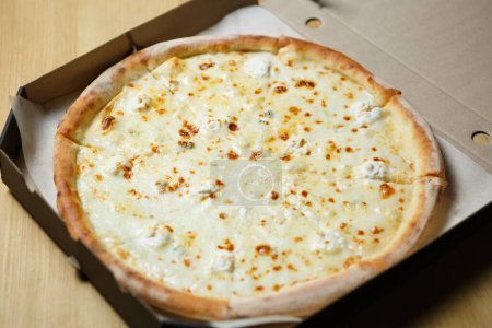 Four cheese pizza delivered in a box. Delicious Italian quattro formaggi dish baked in oven with mozzarella, gorgonzolla, parmesan and blue cheese on crusty bread