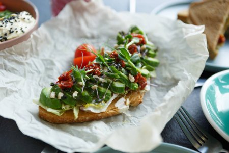 Photo for Gourmet avocado toast served with dried tomatoes and micro greens for breakfast in restaurant - Royalty Free Image