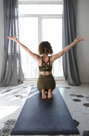 Foto de Hermosa mujer yogui joven estirándose en la alfombra en casa. yogini blanco hembra haciendo ejercicio en el apartamento por la mañana - Imagen libre de derechos