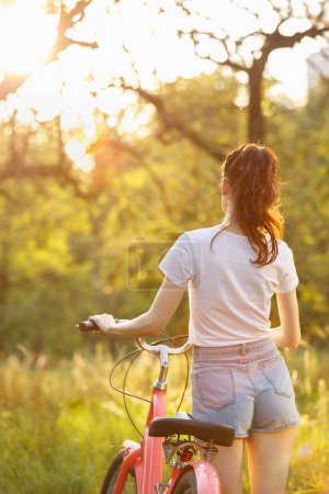 Téléchargez les photos : Jeune femme sexy en short marchant avec un vélo au coucher du soleil. Belle femme blanche chevauchant sur un vélo en plein air dans la journée ensoleillée du printemps - en image libre de droit