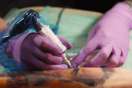 Foto de Tatuaje haciendo un nuevo tatuaje en la piel humana con aguja de la máquina eléctrica. Pistola de tatuaje eléctrica moderna en el trabajo - Imagen libre de derechos