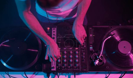 Overhead-Foto von Discjockey Mixing Platten auf einer Party in einem Nachtclub. Professioneller Hip-Hop-DJ spielt Set auf der Bühne, Fokus auf Hände