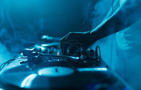 Photo for Night club DJ plays set with vinyl records. Close up photo of professional disc jockey mixing music with turntables and sound mixer in smoke and blue lights - Royalty Free Image