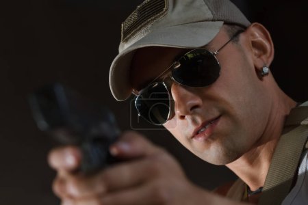 Photo for Cool young Ukrainain soldier aiming the target with a pistol. Portrait of brave white military man in sunglasses shooting with a hand gun - Royalty Free Image
