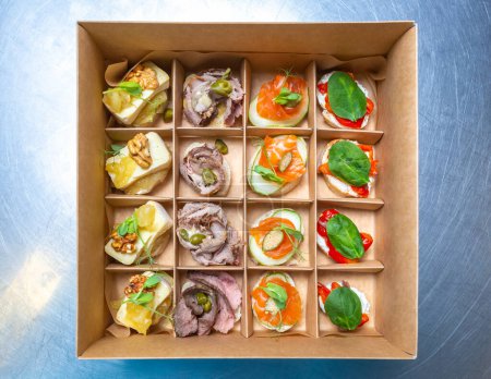 Foto de Caja con aperitivos de vino. Canapés gourmet con ingrediente exótico entregados en caja de cartón para comida catering en el lugar - Imagen libre de derechos