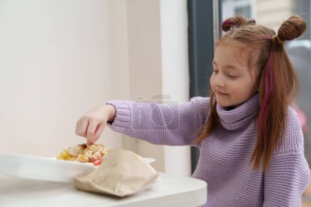 Foto de Linda chica blanca con colas de caballo comiendo souvlaki griego de una lonchera en un café. Lindo niño disfrutando de la comida rápida en un restaurante - Imagen libre de derechos