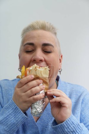 Téléchargez les photos : Portrait de femme adulte affamée aux cheveux courts mangeant des gyros grecs traditionnels avec les yeux fermés - en image libre de droit