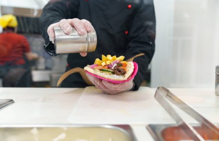 Foto de Cocine vertiendo sal en souvlaki en la cocina. Chef cocina comida rápida griega tradicional para el almuerzo - Imagen libre de derechos