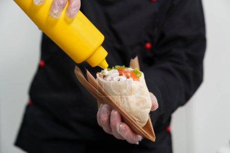 Foto de Chef cocinero verter salsa tzatziki blanco en pita creta merienda en restaurante de comida rápida. Proceso de cocina tradicional griega de comida rápida - Imagen libre de derechos