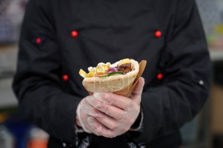Photo for Cook holds gyros wrapped in pita bread. Traditional Greek fast food dish cooked with natural ingredients - grilled chicken meat, fries and white tzatziki sauce - Royalty Free Image