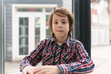 Téléchargez les photos : Mignon garçon d'âge élémentaire assis dans un café. Portrait de joli gamin blanc de 11 ans posant au restaurant - en image libre de droit