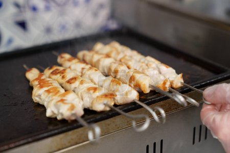 Téléchargez les photos : Le cuisinier tournant la viande de poulet sur des brochettes. Chef préparant filet de volaille marinée sur le gril chaud dans la cuisine du restaurant - en image libre de droit