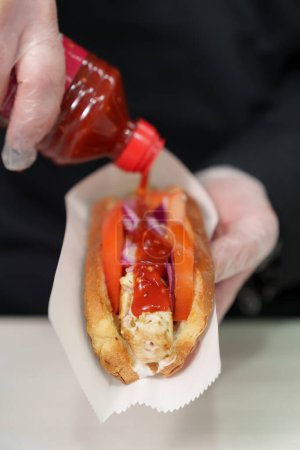 Foto de Cocinar vertiendo salsa asiática picante en hot dog en primer plano. Chef cocinando comida rápida para el almuerzo - Imagen libre de derechos