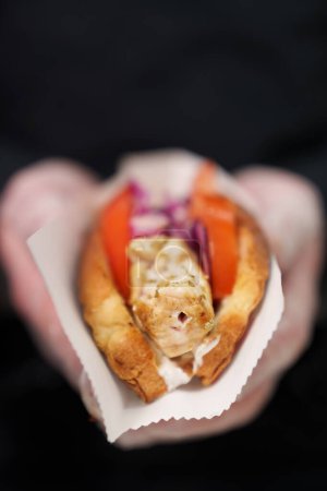 Photo for The cook holding exotic hot dog prepared with marinated chicken meat cooked on grill and served with red onion and hot sauce in crusty buns - Royalty Free Image