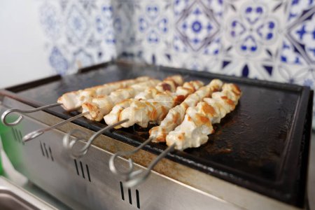 Photo for Chicken meat on skewers cooking on hot grill pan in a Greek fast food restaurant. Close up photo of poultry fillet being cooked for lunch - Royalty Free Image