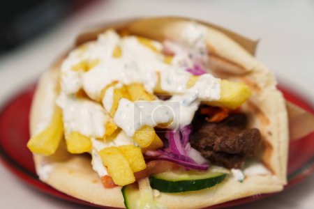 Photo for Delicious Greek gyros served on plate. Traditional pita souvlaki prepared with pita bread, fries and marinated meat covered with white tzatziki sauce - Royalty Free Image
