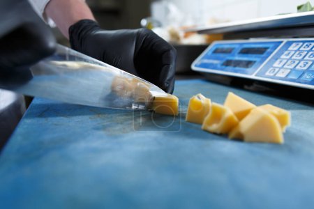 Téléchargez les photos : Cuire des morceaux de fromage gouda jaune avec couteau tranchant sur la planche à découper dans la cuisine commerciale - en image libre de droit