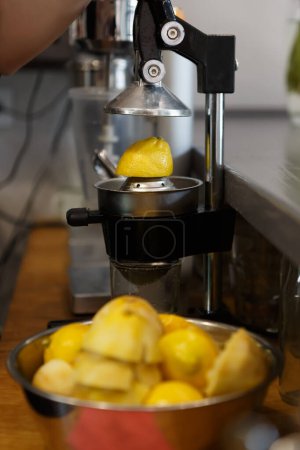 Photo for Bar tender squeezing fresh lemon fruit with manual squeezer machine in close up - Royalty Free Image