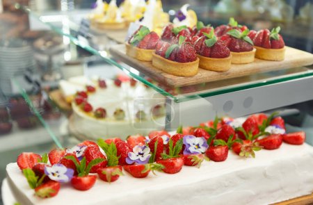 Foto de Delicioso pastel de queso de fresa y pastelitos de tarta con fresas frescas preparadas para el almuerzo en un café de pastelería. No hay gente - Imagen libre de derechos