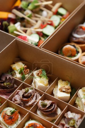 Foto de Los aperitivos de vino se entregan en una caja para la restauración de alimentos en un lugar. Snacks gourmet preparados con deliciosos ingredientes de carne, pescado y queso - Imagen libre de derechos