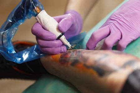 Téléchargez les photos : Tatoueur fait un nouveau dessin sur la jambe du client avec une machine à tatouer électrique moderne en studio - en image libre de droit