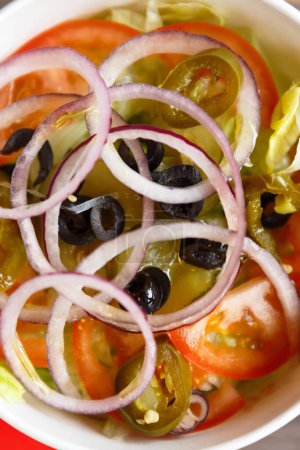 Foto de La ensalada griega en la vajilla para llevar se ha tirado directamente de arriba. Comida vegetariana fresca para el desayuno en una cama plana - Imagen libre de derechos