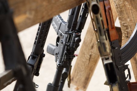 Photo for Weapon stand with assault rifles on a shooting range outdoor. Modern black American machine gun equippped with magnifier scope - Royalty Free Image
