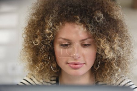 Téléchargez les photos : Portrait de belle femme blanche aux cheveux bouclés à l'aide d'un ordinateur portable à la maison. Jolie femme ukrainienne travaillant sur ordinateur portable avec un sourire - en image libre de droit