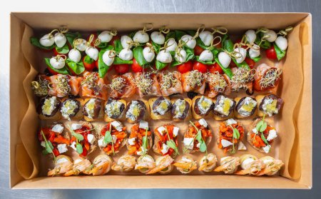 Photo for Large box of gourmet snacks delivered for food catering service on a venue. Big set of delicious canapes prepared for wine party - Royalty Free Image