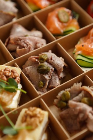 Photo for Delicious appetizer snacks delivered in a cardboard box for food catering on a venue. Bruschetta with veal meat and capers prepared for wine party - Royalty Free Image