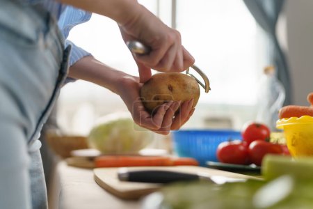 Foto de Persona hembra pelando patatas en primer plano. Mujer cocinando cena vegetariana con verduras - Imagen libre de derechos