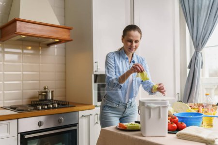 Foto de Mujer blanca alegre hace compost en casa. Casa esposa cocinar el almuerzo y el compostaje de residuos de alimentos orgánicos. Reciclaje responsable de las sobras de una persona femenina en un contenedor de bokashi - Imagen libre de derechos